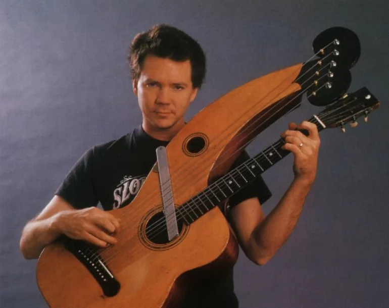 [Michael Hedges holding a harp guitar]