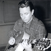 Nappy Lamare sitting and playing guitar while looking down.png